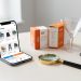Composition réaliste représentant l’optimisation d’un site e-commerce avec un smartphone, des produits, un entonnoir transparent, une loupe et une calculatrice.