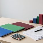 Bureau professionnel présentant trois dossiers vierges de couleurs différentes, une calculatrice, une balance et un graphique abstrait illustrant une décision stratégique après une croissance répétée.