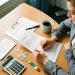 Une consultante organise des factures vierges, des jetons colorés et une calculatrice sur un bureau pour représenter le calcul du coût d’acquisition client d’une agence de services.